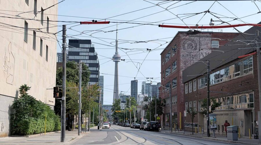 The secret chords of toronto street narrowing to the cn tower in the distance A mass of streetcar wires criss cross in forground